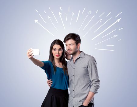 A cheerful young couple taking selfie photo with mobile phone and white lines and arrows pointing to the sky above them concept