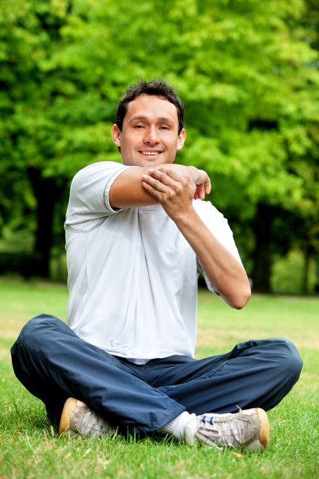 Athletic man sitting outdoors and stretching his arm