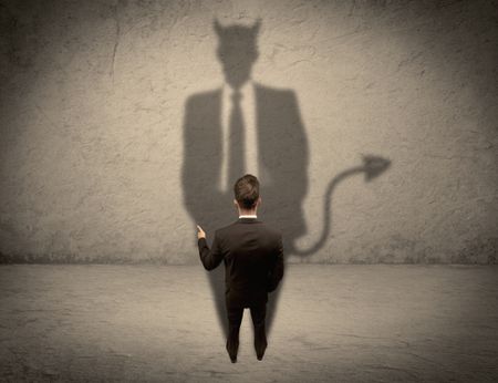 An experienced tricky businessman in suit looking at his devil desguise shadow reflected on the wall concept