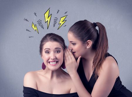 A beautiful girl in black dress sharing secrets to her girlfriend concept with drawn energetic electric yellow signs above her head on the wall background.