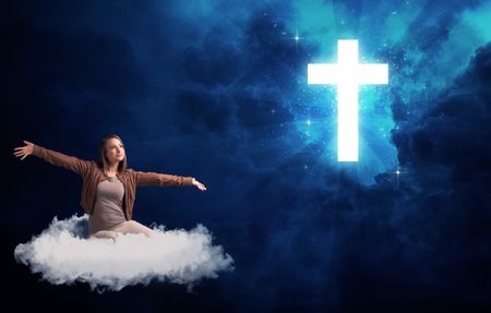 Caucasian woman sitting on a white fluffy cloud looking at a big, bright; blue; glowing cross