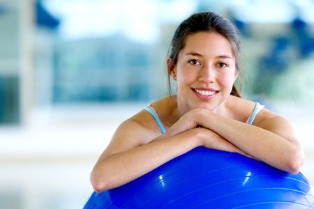 Woman portrait at the gym smiling leaning on a pilates ball