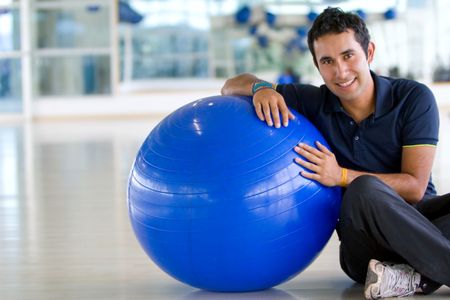 man at the gym leaning on a pilates ball and smiling