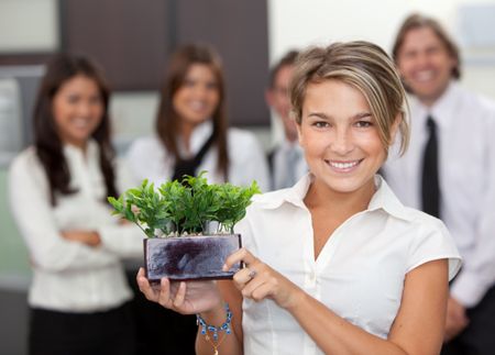 Business woman holding a small tree at the office with a group behind