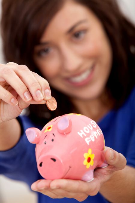 Woman putting a coin into a piggybank for the house budget