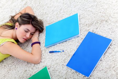 Beautiful female student lying with notebooks at home