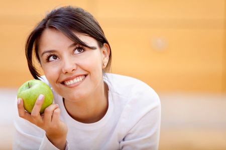 Beautiful pensive woman holding an apple and smiling