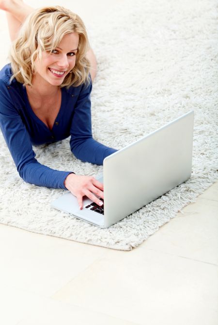 Woman lying on the floor with a laptop computer and smiling