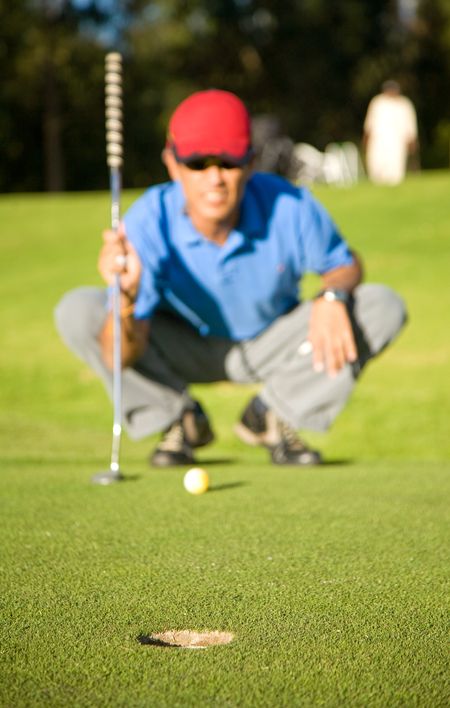 male golfer in a putting green analyzing his shot - focus is on the hole