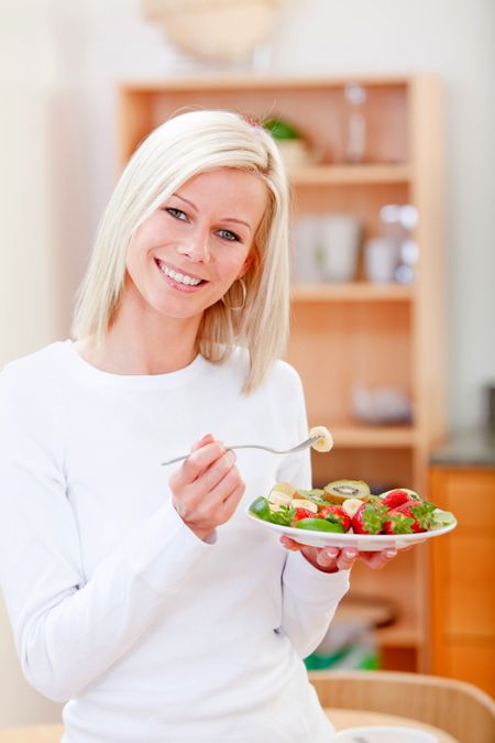 Healthy woman eating fruits at home and smiling