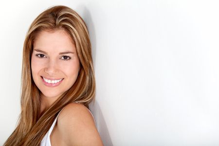 Beautiful woman smiling and leaning on a white wall