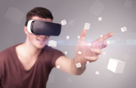 Young impressed man wearing virtual reality goggles with grey cubes around him 