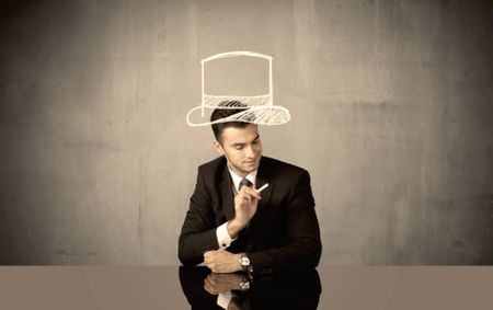 A young happy businessman in elegant suit drawing funny hat and mustache in empty grey space with a chalk illustration concept
