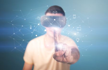 Young impressed man wearing virtual reality goggles with mixed media icons around his finger