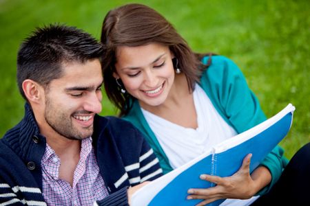 Couple of students holding a notebook outdoors and smiling