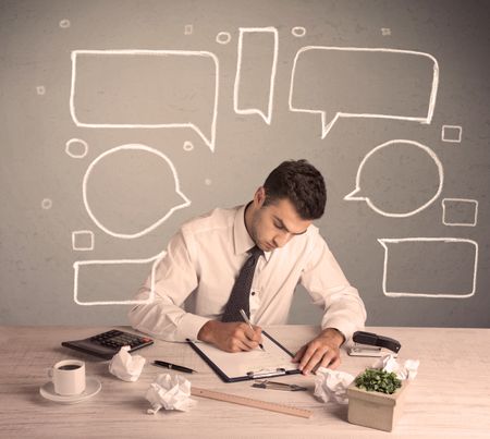 An intelligent elegant business person sitting at a desk and working with drawn empty text bubbles, boxes around him concept