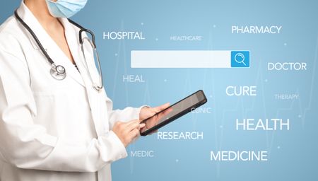 Female doctor holding tablet with blue background and search bar with hovering medical words