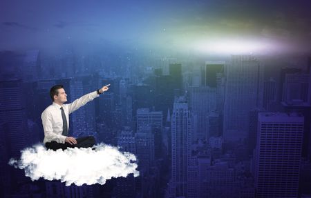 Caucasian businessman sitting on a white fluffy cloud above the city, thinking and wondering