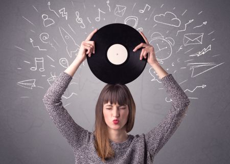 Young lady holding vinyl record on a grey background with mixed scribbles behind her