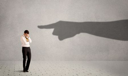 Business person looking at huge shadow hand pointing at him concept on background