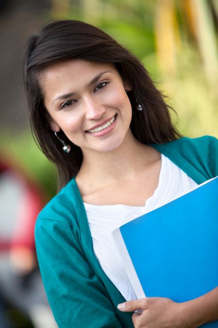 Female student outdoors holding a notebook and smiling