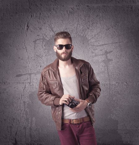 A hipster fashion model guy in casual clothing stnading with mobile phone in front of concrete urban wall background concept