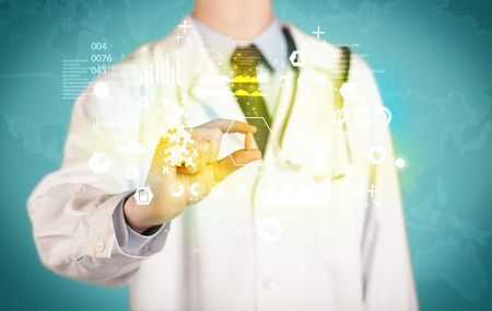 A doctor in white coat with a stethoscope on one shoulder holding a pill with green glowing graphs, lines, numbers, charts, between his fingers