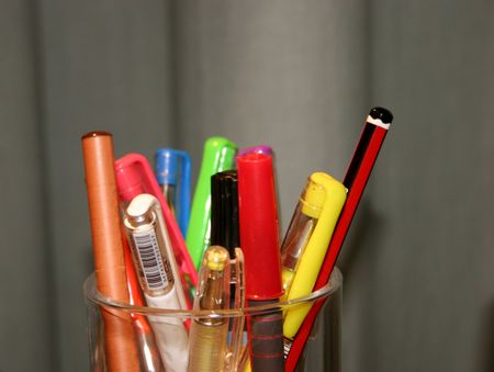 Pens, pencils and markers in a transparent cup