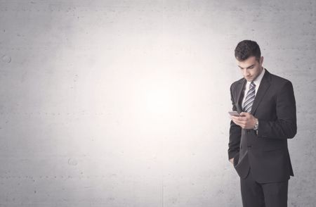 Young sales business person in elegant suit standing in front of clear empty grey wall background while talking on the phone
