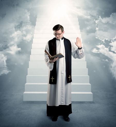 A young religious happy priest standing in front of the stairway to heaven concept with clouds and bright lights coming from above.