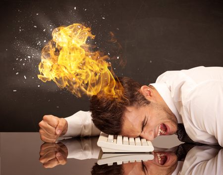 A depressed businessman banging his head in a keyboard and shouting with his head on fire, reflecting on desk