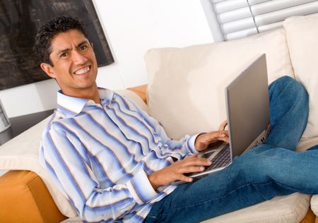 casual entrepreneur working from home looking very relaxed in his sofa browsing the web in his laptop computer