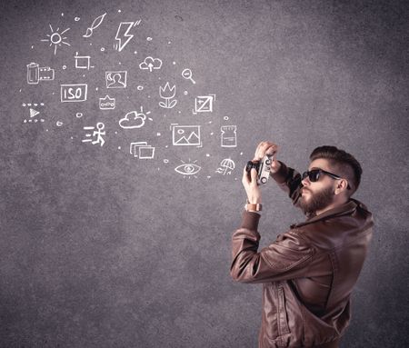 An elegant hipster guy trying to use a vintage camera with camera settings icons drawn on wall, like flash, white balace or ISO value concept
