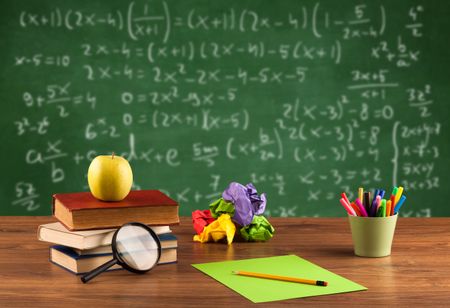 Back to school concept with long numbers calculation on blackboard and a desk with books, fruit