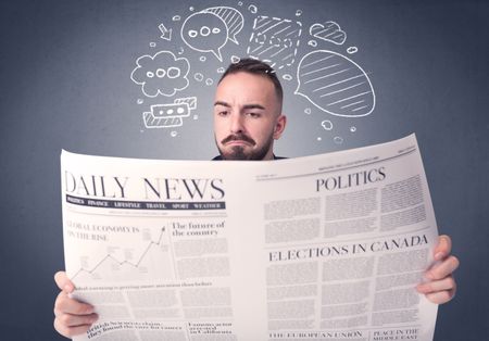Puzzled young businessman reading daily newspaper with speech bubbles above his head