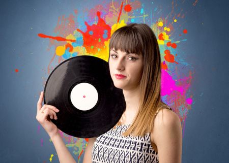 Young lady holding vinyl record on a grey background with colorful splashes behind her 