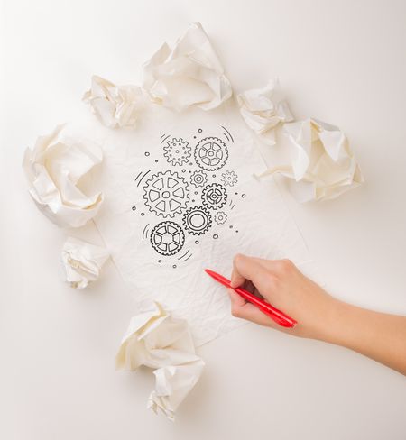 Female hand next to a few crumpled paper balls drawing rotating gears