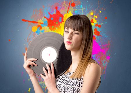 Young lady holding vinyl record on a grey background with colorful splashes behind her 