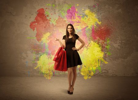 A happy young elegant woman standing with shopping bags in front of brown wall background full of colorful ink splatter concept