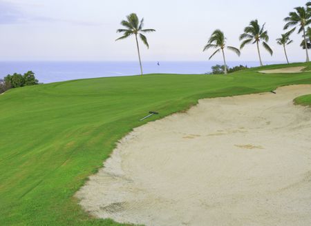 Long sand trap with tire tracks near putting green on oceanside golf course, Big Island of Hawaii