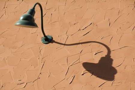Light fixture and its shadow on textured wall near sunset