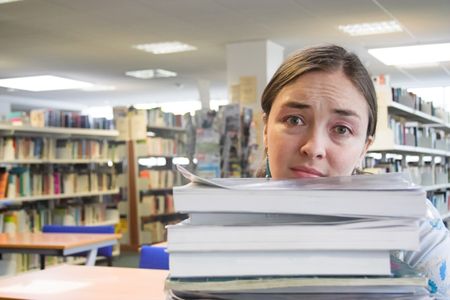 female student in a library with lots of work to do