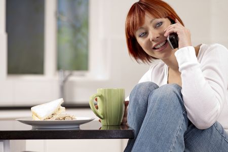 Young femal;e chatting on the phone, while relaxing in her kitchen.