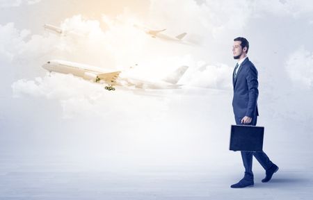 Elegant businessman going somewhere with briefcase and airplane on the background

