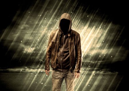 An incognito hooded stalker standing in the rain with his back in front of dark scary landscape concept