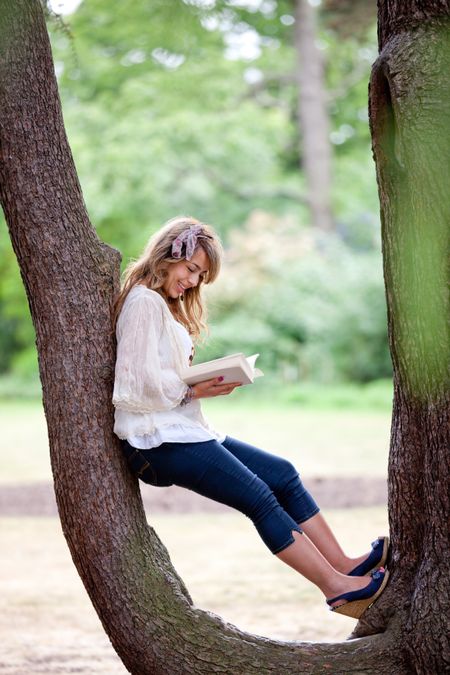 Beautiful woman sitting outdoors on a tree and reading a book