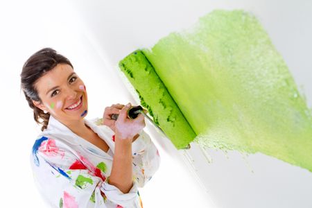 Woman painting a white wall with a roller and smiling
