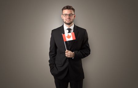 Cheerful student standing in front of wall with national flag on his hand
