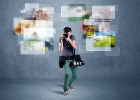 A young professional male photographer holding cameras and taking pictures in front of a blue wall with pictures, icons, text information concept