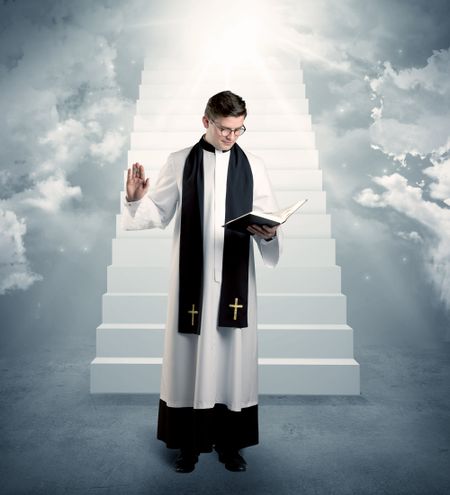 A young religious happy priest standing in front of the stairway to heaven concept with clouds and bright lights coming from above.